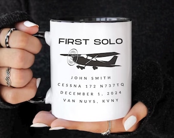 May include: White ceramic mug with a black rim and handle. The mug features a black silhouette of a small airplane with the text "FIRST SOLO" above it. Below the airplane is the text "JOHN SMITH", "CESSNA 172 N737TQ", "DECEMBER 1, 2024", and "VAN NUYS, KVNY".