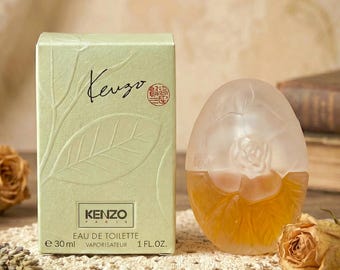 May include: A Kenzo Paris Eau de Toilette perfume bottle and box. The box is light green with leaf illustrations and the Kenzo logo. The perfume bottle is egg-shaped with a frosted rose design. The bottle contains 1 fl. oz. of perfume.
