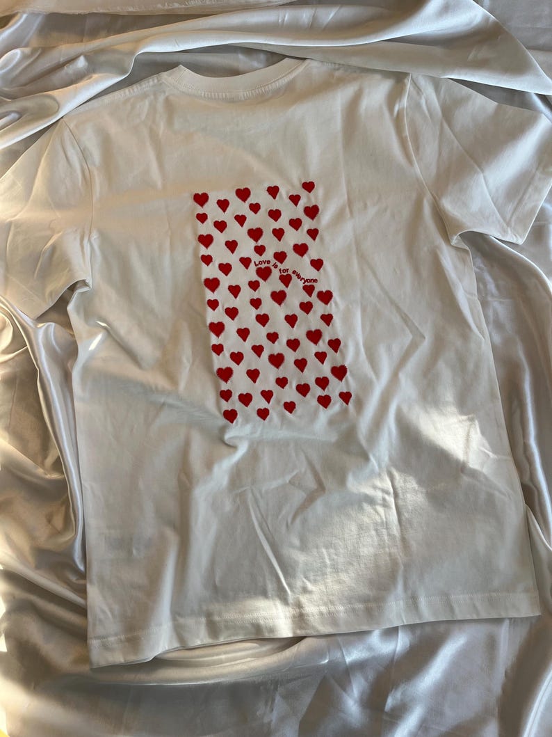 May include: White t-shirt with a red heart pattern and the text "Love is for everyone" printed on the back.
