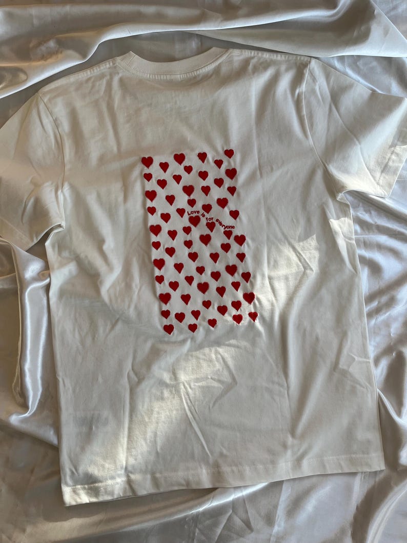 May include: White t-shirt with a red heart pattern and the text "Love for everyone" on the back.