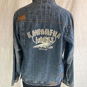 Könnte beinhalten: Eine blaue Jeansjacke mit einem weißen gestickten Aufnäher auf der Rückseite, auf dem "Kawartha Lakes Loyal to the Game Rough & Raw" steht.