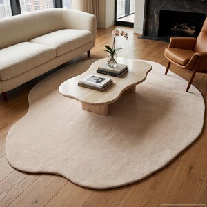Könnte beinhalten: Ein unregelmäßig geformter Teppich in hellem Beige mit einer flachen Florstruktur. Der Teppich ist aus handgewebter neuseeländischer Wolle gefertigt und weist eine weiche, abgerundete Silhouette auf, die einen Teil des Holzbodens bedeckt.