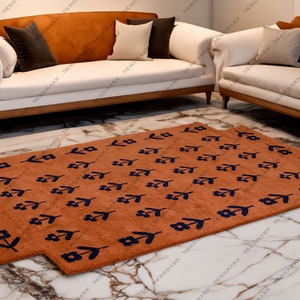 May include: Two rectangular, rust-colored rugs with a floral pattern in navy blue are displayed on a marble floor. The rugs are in front of a white sofa with wooden legs and a brown back.