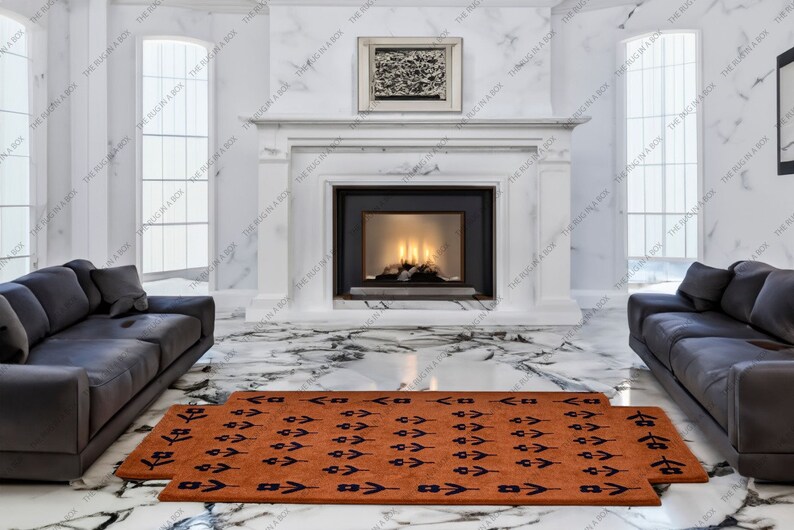 May include: Two terracotta-colored rugs with a repeating navy blue arrow and geometric pattern are displayed in front of a fireplace. The rugs are rectangular and placed on a marble floor. The room has a modern design.