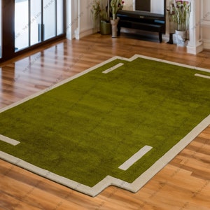 May include: A rectangular green rug with a light beige border and geometric design. The rug has a plush texture and is placed on a hardwood floor. The rug's design includes rectangular accents within the border.