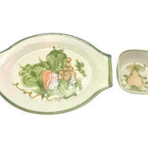 May include: Two-piece ceramic serving set. The set includes an oval platter with handles and a square bowl. Both pieces are off-white with green and peach-colored fruit and leaf designs. The rims are outlined in green.