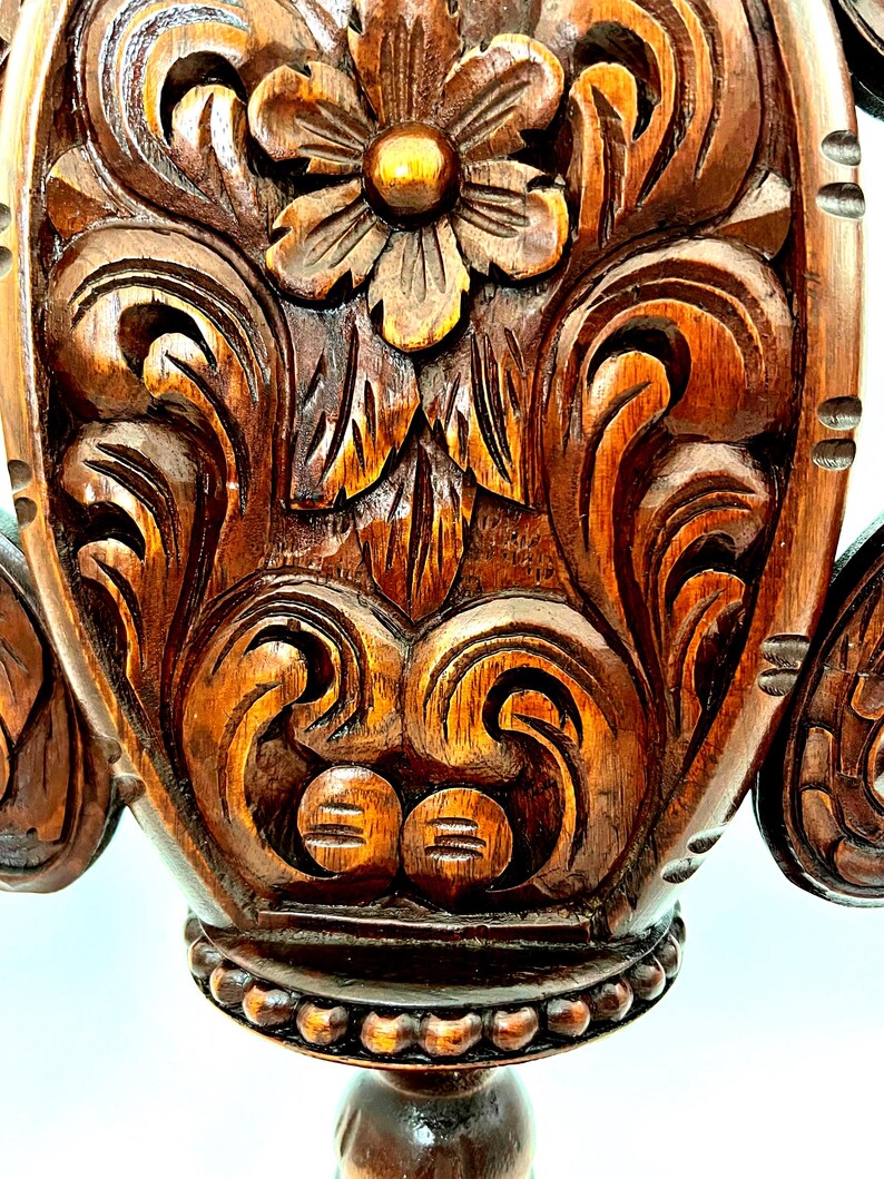 Puede incluir: Primer plano de un detalle de mueble de madera ricamente tallado. La madera marr&oacute;n oscuro presenta intrincados dise&ntilde;os florales y de volutas, con una flor prominente en el centro. El tallado tiene un efecto tridimensional, mostrando la artesan&iacute;a.