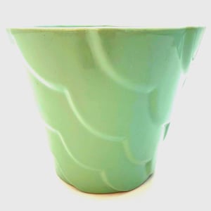 May include: A light green ceramic vase with a unique, wavy design. The vase has a flared top and a textured surface, adding visual interest. The soft green color gives it a fresh, modern look, suitable for displaying flowers or as a decorative piece.