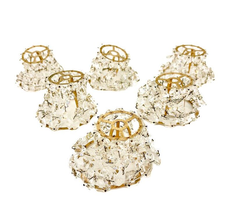 May include: Six vintage crystal chandelier shades with gold-toned metal frames. The shades are covered in clear, faceted crystals, creating a sparkling effect. The shades are designed to diffuse light and add a touch of elegance to any room.