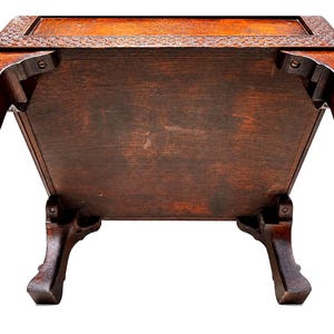May include: A dark brown wooden table with ornate carved details on the top edge and legs. The table has a rectangular shape with a visible underside, showcasing the wood grain and construction. The legs are curved and add a decorative element.