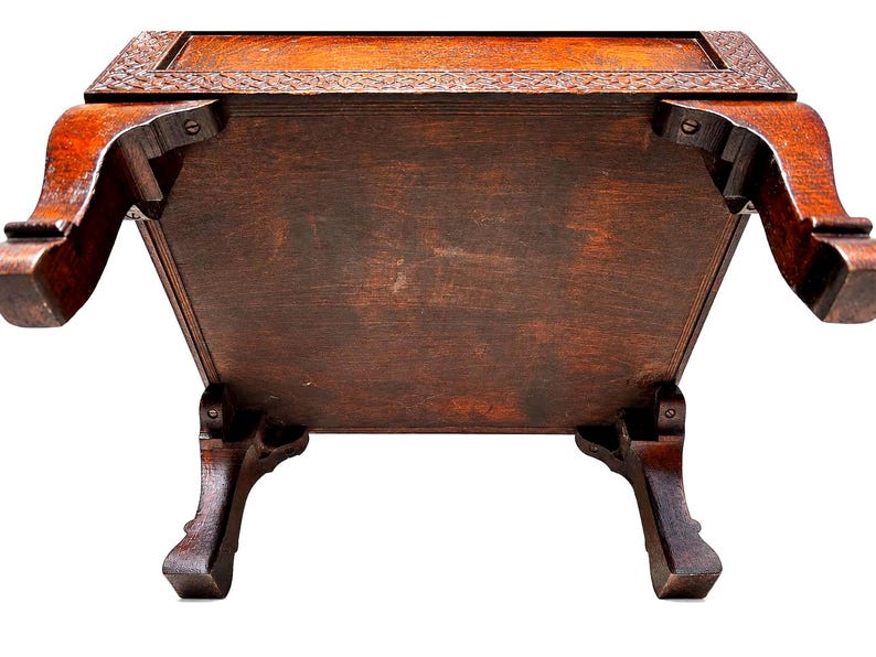 May include: A dark brown wooden table with ornate carved details on the top edge and legs. The table has a rectangular shape with a visible underside, showcasing the wood grain and construction. The legs are curved and add a decorative element.