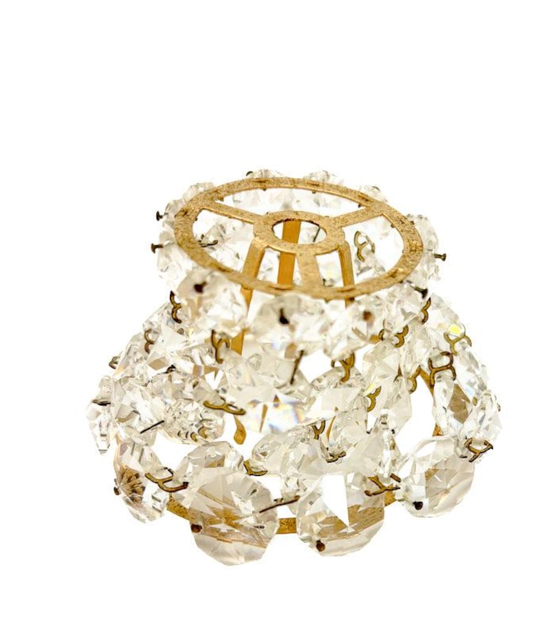 May include: A small, vintage chandelier lampshade with a gold-colored metal frame. The shade is adorned with numerous clear, faceted crystal beads, creating a sparkling, elegant appearance. The design is reminiscent of antique lighting fixtures.