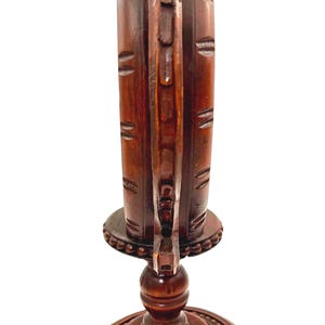 Puede incluir: Un jarr&oacute;n de madera tallada de color marr&oacute;n oscuro con un asa decorativa. El jarr&oacute;n tiene una base ancha y redonda y una parte superior acampanada. La madera tiene un rico color marr&oacute;n rojizo y est&aacute; intrincadamente tallada con l&iacute;neas y patrones verticales.
