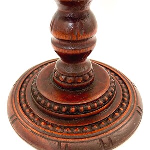 Puede incluir: Primer plano de un pedestal de madera tallada de color marr&oacute;n oscuro. El pedestal tiene una base redonda con un borde de cuentas y una columna torneada detallada. La madera tiene un acabado rico y pulido, mostrando las intrincadas tallas.