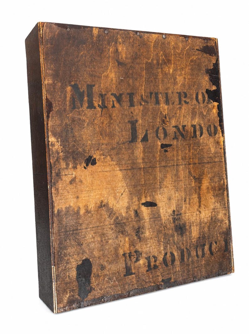 May include: A vintage wooden box with dark brown staining and black stenciled text. The text reads "MINISTERO LONDON" and "1st PRODUCT". The box has a rectangular shape and is likely an antique.