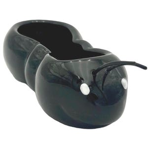 May include: A glossy black ceramic planter shaped like an ant. The planter has a large opening for plants, white dot eyes, and curved antennae. The ant planter is a decorative item for home or garden.