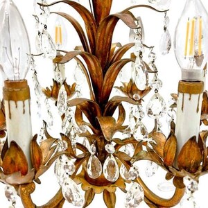 May include: Close-up of a vintage gold-toned chandelier with clear crystal accents. The chandelier features a floral design with multiple light fixtures and decorative crystal droplets. The bulbs are clear and have a warm glow.
