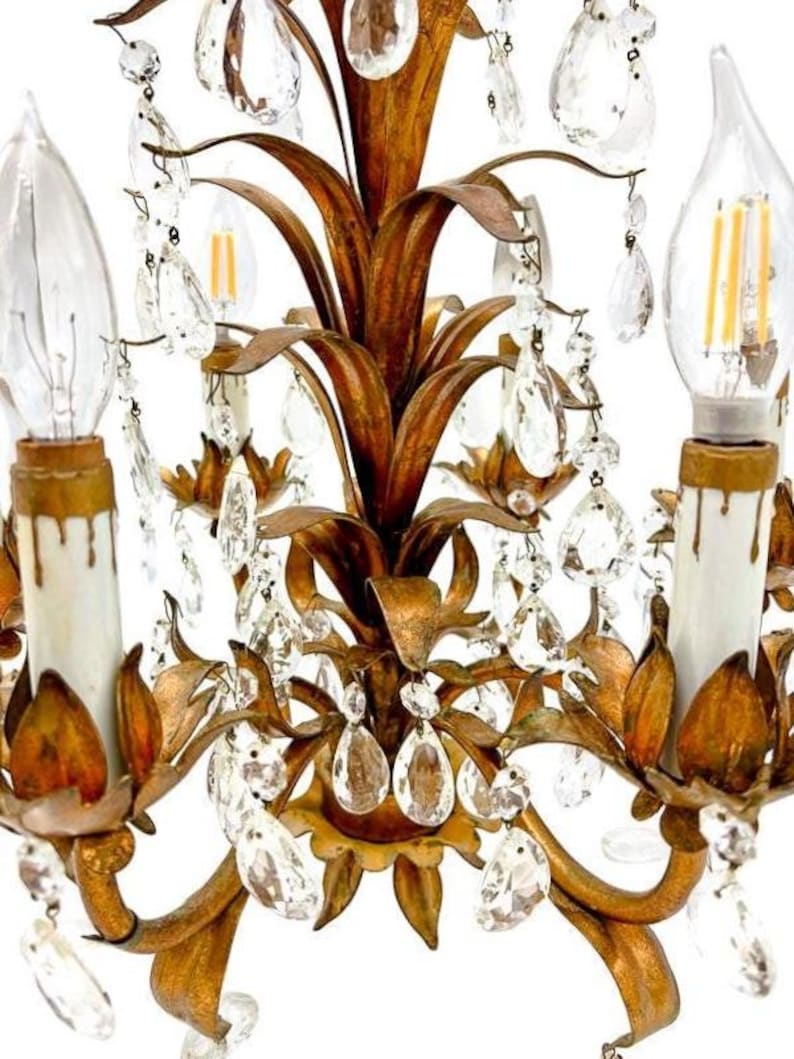 May include: Close-up of a vintage gold-toned chandelier with clear crystal accents. The chandelier features a floral design with multiple light fixtures and decorative crystal droplets. The bulbs are clear and have a warm glow.