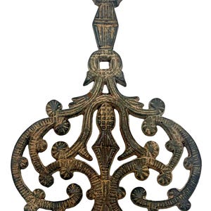 May include: Ornate, cast iron trivet with a dark bronze finish. The trivet features an intricate, openwork design with scrolling patterns and a decorative top. A functional and decorative kitchen accessory.