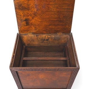 May include: A wooden storage chest with a hinged lid, open to reveal interior compartments. The chest is stained a warm brown color, with decorative carvings along the front and sides. It rests on short, square feet.