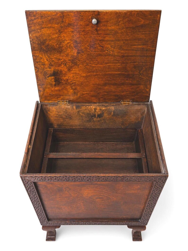 May include: A wooden storage chest with a hinged lid, open to reveal interior compartments. The chest is stained a warm brown color, with decorative carvings along the front and sides. It rests on short, square feet.