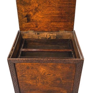 May include: Open wooden chest with a hinged lid, showcasing a rich, warm brown finish. The chest features decorative carved detailing around the edges and rests on short, sturdy legs. The interior reveals compartments, suggesting storage for various items.