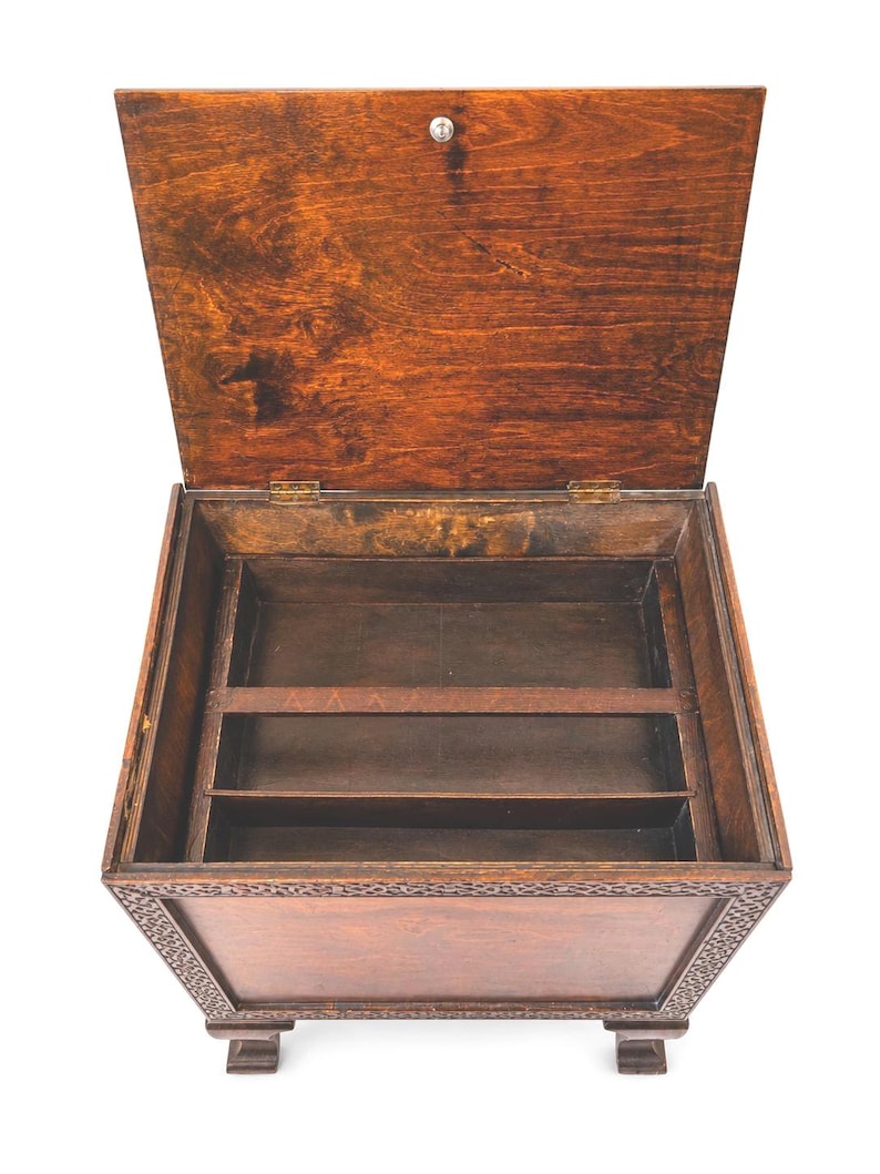 May include: A wooden box with a hinged lid, open to reveal interior compartments. The box is stained a warm brown color, with decorative carvings around the edges. The lid is slightly ajar, showing the interior storage space.