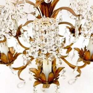 May include: Close-up of a vintage chandelier with a gold-toned metal frame and numerous crystal accents. The chandelier features multiple arms with candle-style light fixtures and dangling crystal pendants, creating a glamorous and elegant aesthetic.