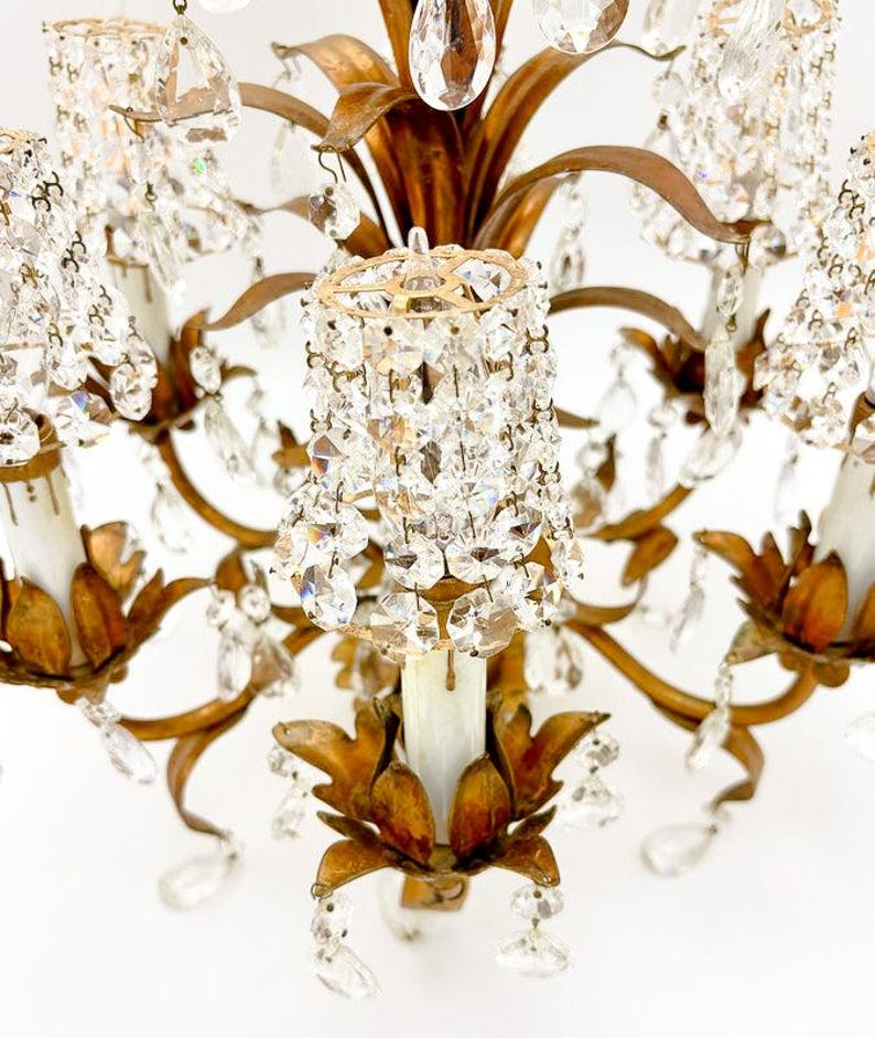 May include: Close-up of a vintage chandelier with a gold-toned metal frame and numerous crystal accents. The chandelier features multiple arms with candle-style light fixtures and dangling crystal pendants, creating a glamorous and elegant aesthetic.