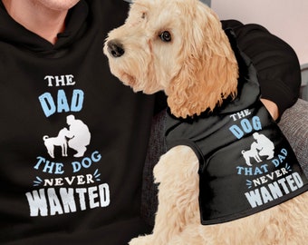 May include: A black hoodie with the text "The Dad The Dog Never Wanted" in white and blue lettering. A dog wearing a black vest with the text "The Dog That Dad Never Wanted" in white and blue lettering.
