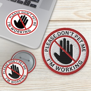 Op de afbeelding: Een verzameling ronde items met de tekst "PLEASE DON'T PET ME I'M WORKING". Inclusief een sticker op een laptop, een patch en een button. Het ontwerp toont een zwarte hand in een rode cirkel met een rode streep erdoor.