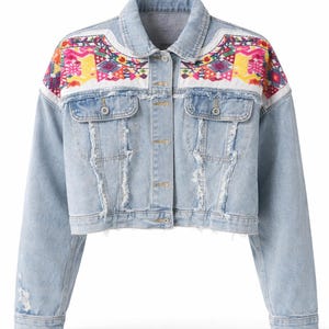 Könnte beinhalten: Hellblaue Jeansjacke mit farbenfrohen Stickereien auf Schultern und Brust. Die Jacke hat einen Used-Look mit Rissen und Knopfverschlüssen. Ein stilvolles Oberbekleidungsstück.