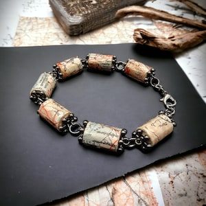 Könnte beinhalten: Ein Armband aus aufgerollten Vintage-Karten mit silbernen Metallakzenten. Das Armband besteht aus sechs Kartenabschnitten und einer silbernen Kette.