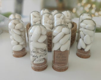 May include: Clear glass tubes filled with white candies, each sealed with a cork base. Some tubes have labels with text, including names and dates. A woven basket holds additional tubes.