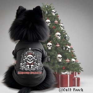 May include: A black dog wearing a black shirt with a graphic of a dog in a Santa hat surrounded by skulls, with the text "HARDCORE HOLIDAYS." A Christmas tree decorated with skull ornaments and red and white striped baubles is in the background.