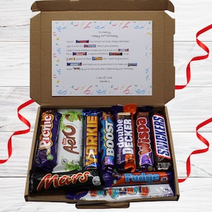 May include: A selection of chocolate bars in a gift box, including Picnic, Aero, and Yorkie. The box has a birthday card with a message. The box is brown with a white background and red ribbon.