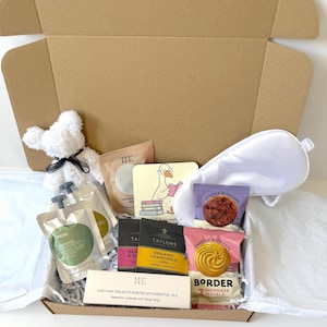 May include: A gift box containing a white plush bear, a white sleep mask, a square coaster with a goose reading books, two small pouches of bath soak, two tea bags, and a package of Border Viennese Whirls biscuits, plus a box of 3 soy wax tealights.