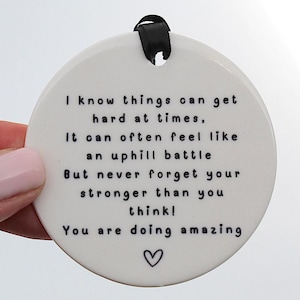 May include: White ceramic round ornament with black text that reads: "I know things can get hard at times. It can often feel like an uphill battle But never forget your stronger than you think! You are doing amazing ♡"