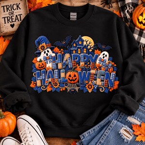 May include: A black crewneck sweatshirt featuring a graphic print with the text "HAPPY HALLOWEEN" in blue and tan plaid letters. The design includes ghosts, pumpkins, a haunted house, bats, sunflowers, and a spider web on a dark background.