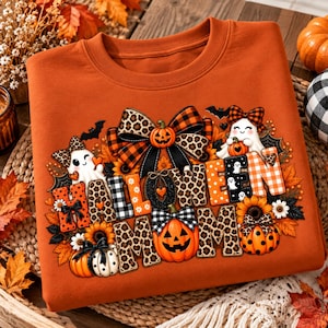 May include: An orange crewneck sweatshirt featuring a graphic print that reads HALLOWEEN MOM. The design includes pumpkins, ghosts, sunflowers, bats, and bows with leopard print and plaid patterns in orange, black, and white colors.
