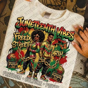 May include: Cream-colored sweatshirt with a vibrant graphic design. The design features two figures, text that reads "Juneteenth Vibes", "Freedom Street", and other phrases. The artwork includes chains, butterflies, and boomboxes.
