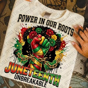 May include: Cream-colored sweatshirt with a vibrant graphic celebrating Juneteenth. The design features a clenched fist in Pan-African colors, a woman's silhouette, flowers, and the text "POWER IN OUR ROOTS" and "JUNETEENTH UNBREAKABLE".