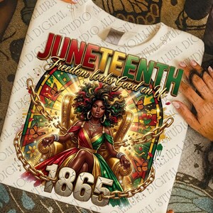 May include: Cream-colored sweatshirt featuring a vibrant Juneteenth design. The graphic includes the text "Juneteenth" and "Freedom looks Good on Us", along with an illustration of a woman in a red, green, and gold dress, seated on a throne. Gold chains and butterflies surround the central image, with the year "1865" at the bottom.