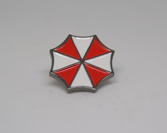 May include: A red and white enamel pin featuring the Umbrella Corporation logo from the Resident Evil video game series.
