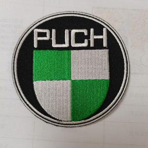 Pode incluir: Patch bordado circular com a palavra "PUCH" em letras brancas. O patch tem uma borda preta e um contorno branco, com um design de escudo quadriculado verde e branco.