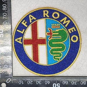Op de afbeelding: Geborduurde patch met het Alfa Romeo-logo. De cirkelvormige patch heeft een blauwe rand met gouden afwerking. Het logo bevat een rood kruis op een witte achtergrond en een groene slang met een kroon.
