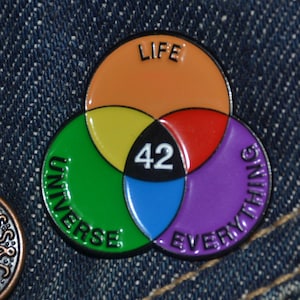 May include: A colorful enamel pin featuring a Venn diagram design. The overlapping circles are orange, green, red, purple, yellow, and blue, with the words "LIFE", "UNIVERSE", and "EVERYTHING". The number "42" is in the center.