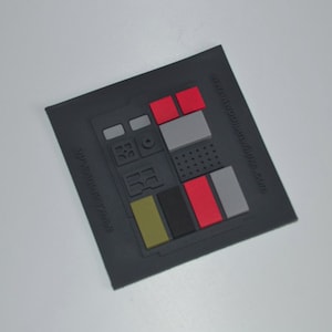 Könnte beinhalten: Ein schwarzer Gummiflicken mit einem grauen, roten und gelben Design. Der Patch verfügt über eine Reihe von Knöpfen und einen kleinen Kreis in der Mitte. Der Text "www.mobilewinks.com" ist auf dem Patch aufgedruckt.