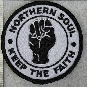 Op de afbeelding: Ronde patch met een zwart-wit ontwerp. De patch heeft een vuist in het midden, omringd door de woorden "NORTHERN SOUL" en "KEEP THE FAITH" in zwarte tekst. De patch heeft een zwarte rand.