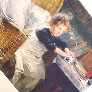 以下が含まれることがあります： 白いドレスと黒いセーターを着た若い女の子が、籐のバスケットに座って、葉のついた小さな枝を持っています。女の子は長い茶色の髪をしていて、枝を見下ろしています。背景は素朴な木製の壁です。